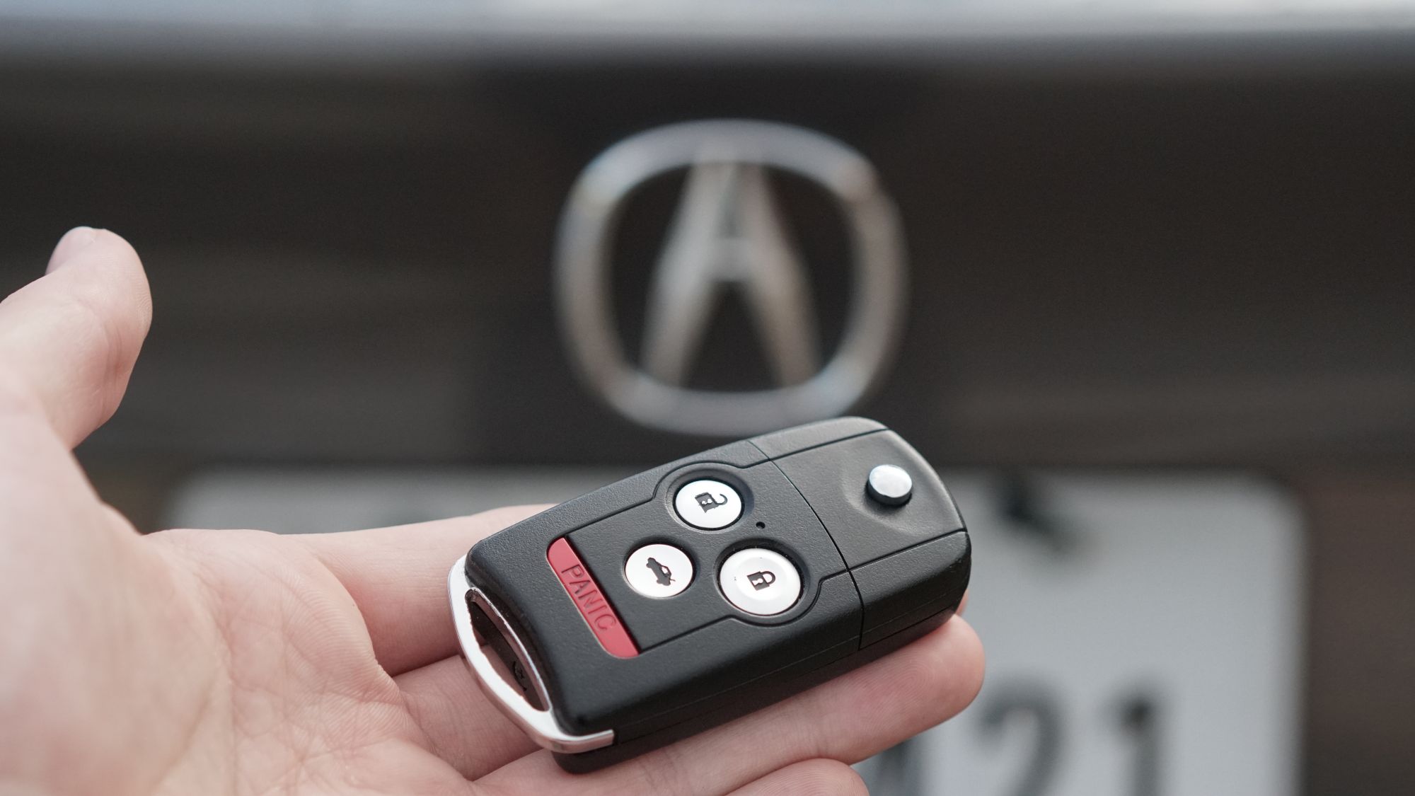 Hand holding a black Acura key fob in front of the Acura emblem