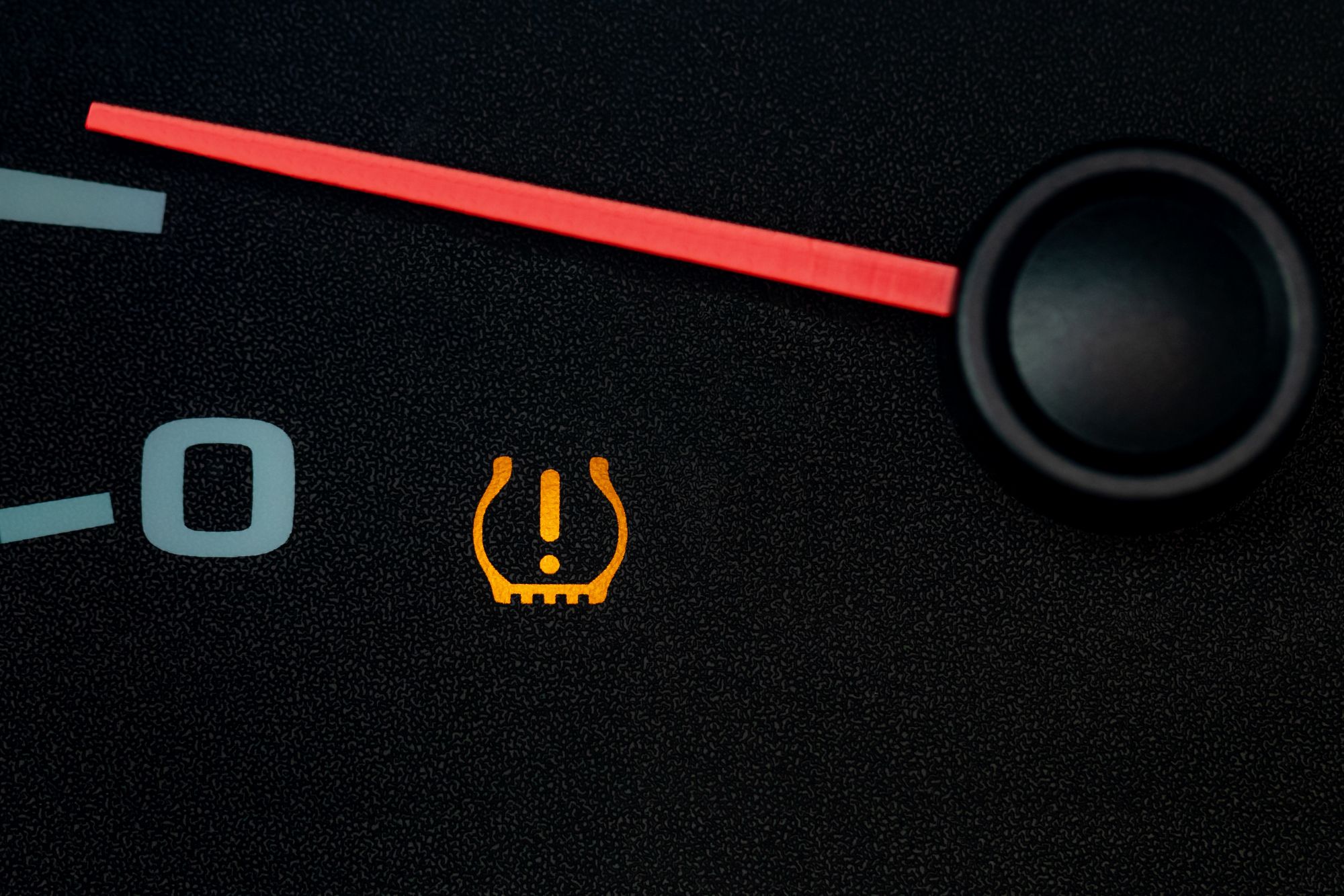 Amber Mazda tire pressure light with an exclamation point lit on a dark dashboard