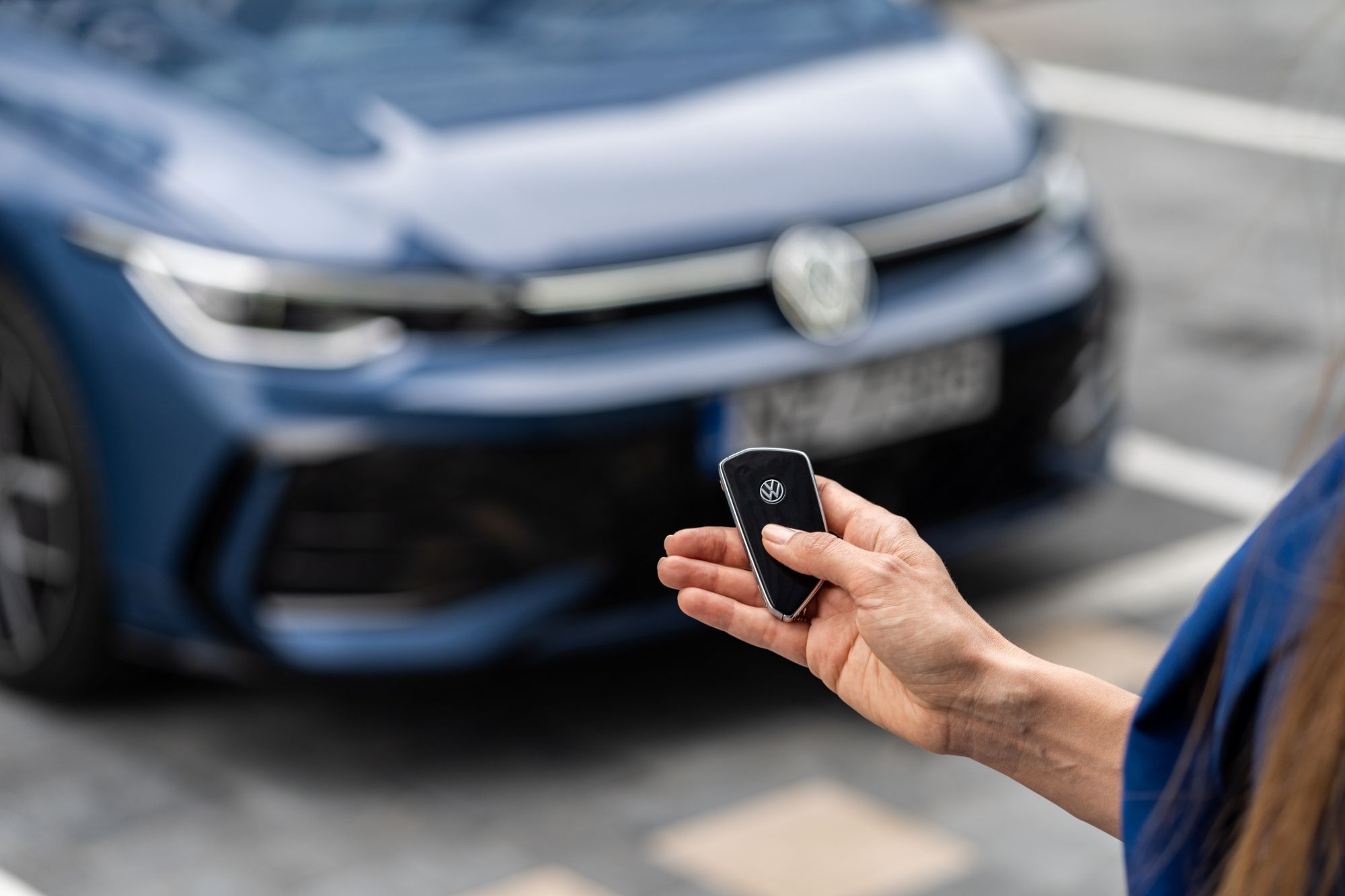 Person holding a Volkswagen key fob in front of a blue Volkswagen